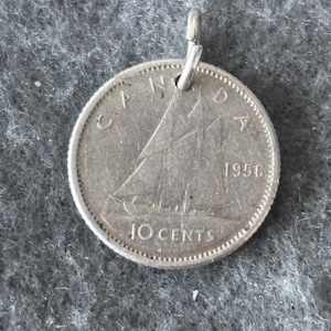 Puede incluir: Colgante de plata hecho con una moneda canadiense de 10 centavos de 1956. La moneda presenta un diseño de velero y la palabra «CANADA». Se adjunta un pequeño lazo plateado para colgar. Mide aproximadamente 2,3 cm de diámetro.