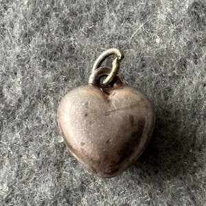 May include: A silver heart-shaped charm with a loop for attaching to a necklace or bracelet.