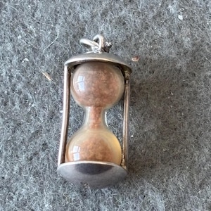 May include: A silver hourglass pendant with a clear glass bulb filled with brown sand.