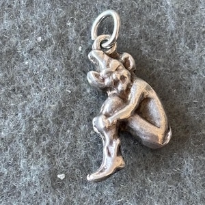 May include: A silver charm in the shape of a sitting gargoyle with a wide open mouth.