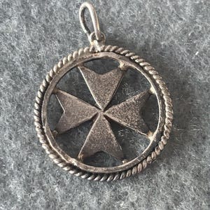 May include: Silver pendant featuring a Maltese cross design. The cross is encircled by a rope-like border.