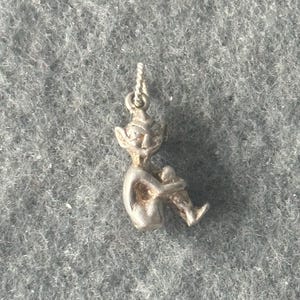 May include: Silver charm of a small, sitting, mythical creature with pointed ears and a mischievous expression.
