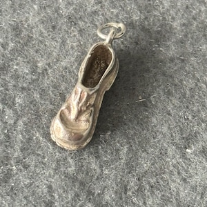 Puede incluir: Encanto de plata con forma de zapato. El zapato tiene un diseño detallado y un bucle en la parte superior para sujetarlo a una pulsera o collar.