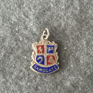 Puede incluir: Encanto de plata con un escudo de esmalte azul y rojo con un escudo de armas y la palabra "RAMSGATE" en la parte inferior.