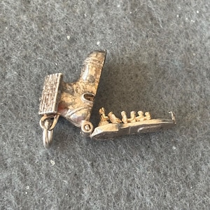 Puede incluir: Encanto de plata en forma de bota con una tapa con bisagras que se abre para revelar un grupo de pequeñas figuras en el interior. El encanto está detallado con una superficie texturizada y un pequeño bucle para sujetarlo a una pulsera o collar.
