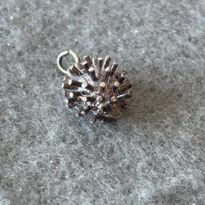 May include: A silver charm in the shape of a spiky ball with a loop at the top for attaching to a bracelet or necklace.