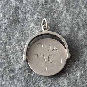 Peut inclure: Pendentif argenté avec un charme circulaire rotatif. Le charme porte des symboles gravés et est suspendu dans un cadre incurvé. Bijou conçu pour être porté.