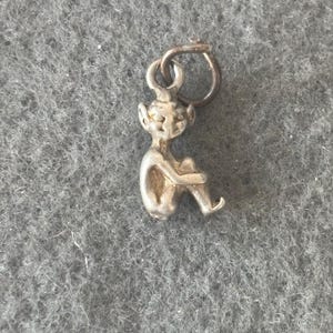 May include: A silver charm in the shape of a sitting fairy with a pointed hat and large ears.