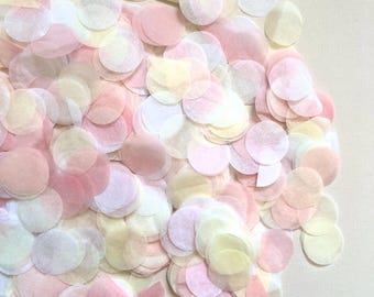 Peut inclure: Une collection de confettis en papier circulaires dans des tons pastel doux de rose pâle, crème, blanc et jaune clair. Les disques de papier fins et translucides sont dispersés dans un arrangement dense et superposé, créant une texture.