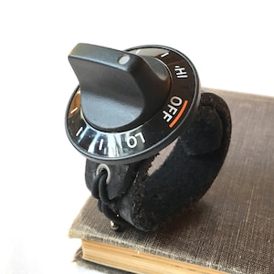 May include: A black rotary switch with a dial that reads "LO", "HI", and "OFF". The switch is attached to a black leather strap.