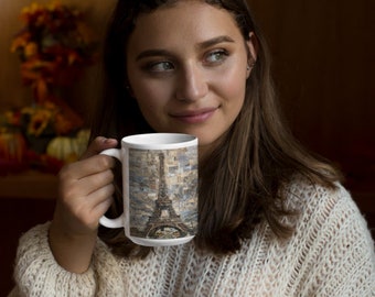 May include: A white ceramic mug featuring a detailed graphic print of the Eiffel Tower. The tower is depicted against a textured, mosaic-style background composed of various shades of blue, beige, and brown, creating a layered visual effect.