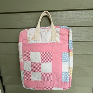 May include: A pink quilted tote bag with a patchwork design featuring various floral and geometric patterns. The bag has a cream-colored fabric handle.