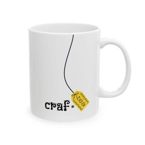 May include: White ceramic mug with a black line and a yellow tea bag tag that reads "R-tea". The mug also has the word "craf*" printed on it in black, whimsical lettering. The mug has a white handle.