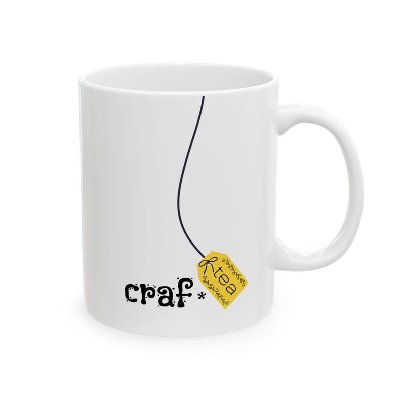 May include: White ceramic mug with a black line and a yellow tea bag tag that reads "R-tea". The mug also has the word "craf*" printed on it in black, whimsical lettering. The mug has a white handle.