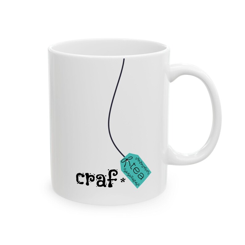 May include: White ceramic mug with a black line and a teal tag that says "R-tea". The mug also has the word "craf*" printed on it in a whimsical font. The mug has a curved handle.