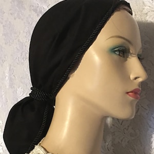 May include: Black fabric hair covering with a black rope trim. The fabric is gathered at the back and tied into a bun.