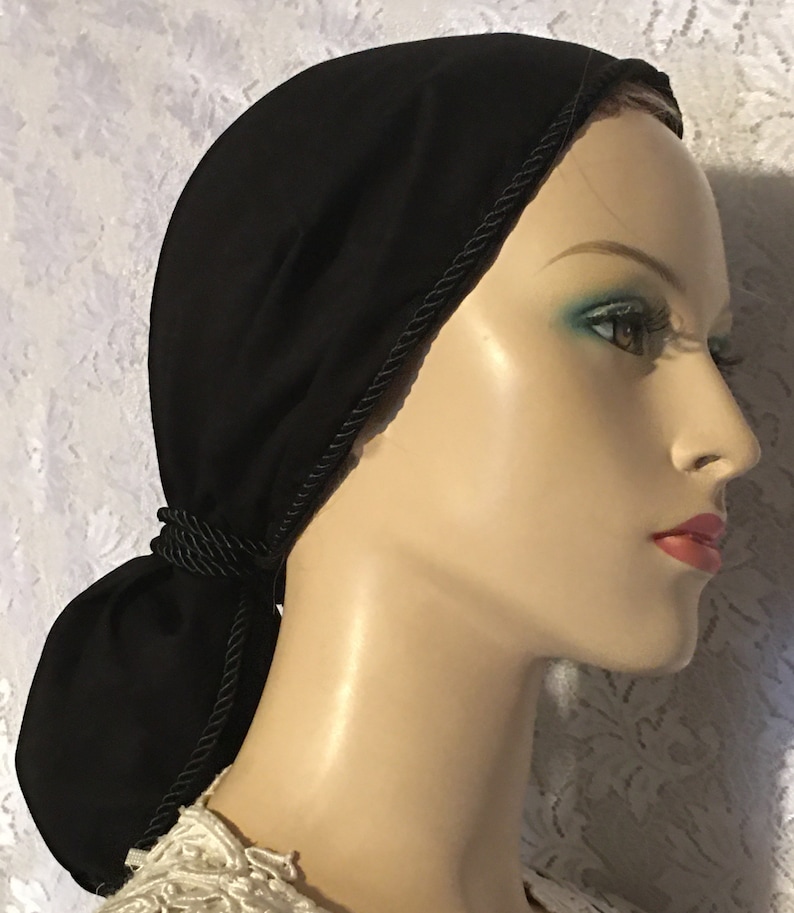 May include: Black fabric hair covering with a black rope trim. The fabric is gathered at the back and tied into a bun.