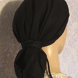 May include: Black fabric head covering with a black rope tie. The fabric is gathered at the back and tied into a bun shape.
