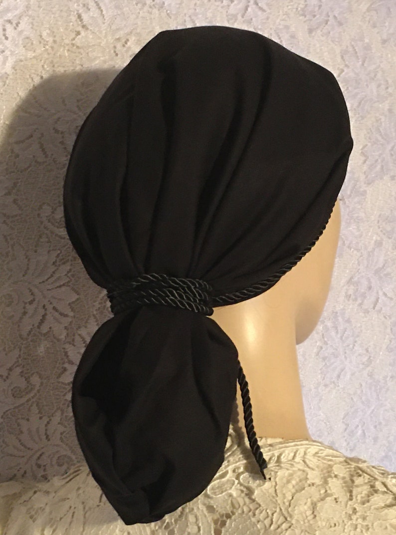 May include: Black fabric head covering with a black rope tie. The fabric is gathered at the back and tied into a bun shape.