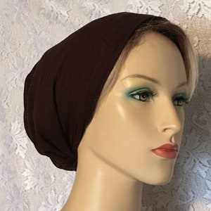Peut inclure: Un bandeau de tête en tissu marron, porté sur une tête de mannequin. Le bandeau est fait d'un matériau doux et extensible et est conçu pour être porté comme un turban ou un foulard.