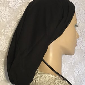 May include: Black satin sleep cap with a black satin drawstring and black trim. The cap is worn on a mannequin head.