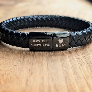 Personalized Black Leather Bracelet for Men – Engraved Magnetic Clasp | Custom Gift for Husband, Boyfriend or Dad, Custom Father's Day name. Handcrafted from genuine black braided leather with a sleek engraved black clasp, this personalized bracelet is rugged, refined, and ridiculously handsome. Close-up of a black braided leather bracelet featuring engraved black metal plates. One plate reads “Have Fun Always Love,” and the other is personalized with the name “Ellie” and a heart symbol.