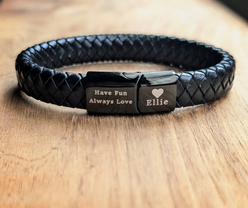 Personalized Black Leather Bracelet for Men – Engraved Magnetic Clasp | Custom Gift for Husband, Boyfriend or Dad, Custom Father's Day name. Handcrafted from genuine black braided leather with a sleek engraved black clasp, this personalized bracelet is rugged, refined, and ridiculously handsome. Close-up of a black braided leather bracelet featuring engraved black metal plates. One plate reads “Have Fun Always Love,” and the other is personalized with the name “Ellie” and a heart symbol.