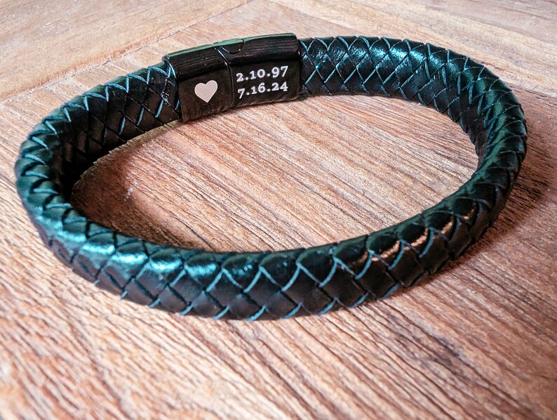 Personalized Black Leather Bracelet for Men – Engraved Magnetic Clasp | Custom Gift for Husband, Boyfriend or Dad, Custom Father's Day name. Whether you're engraving your kids' names, an anniversary date, or a private message tucked discreetly inside, this bracelet brings sentimental value to a piece he’ll actually want to wear. A black leather bracelet with a braided design and a silver clasp. The clasp has a heart engraved on it and the text '2.10.97 7.16.24'.