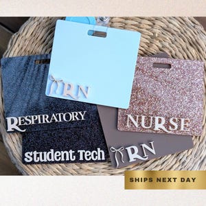 Può includere: Una collezione di porta badge rettangolari in vari colori, tra cui azzurro, grigio e marrone, con accenti glitterati. Ogni porta badge presenta scritte bianche che indicano titoli professionali come "Respiratory", "Nurse" e "Student Tech".