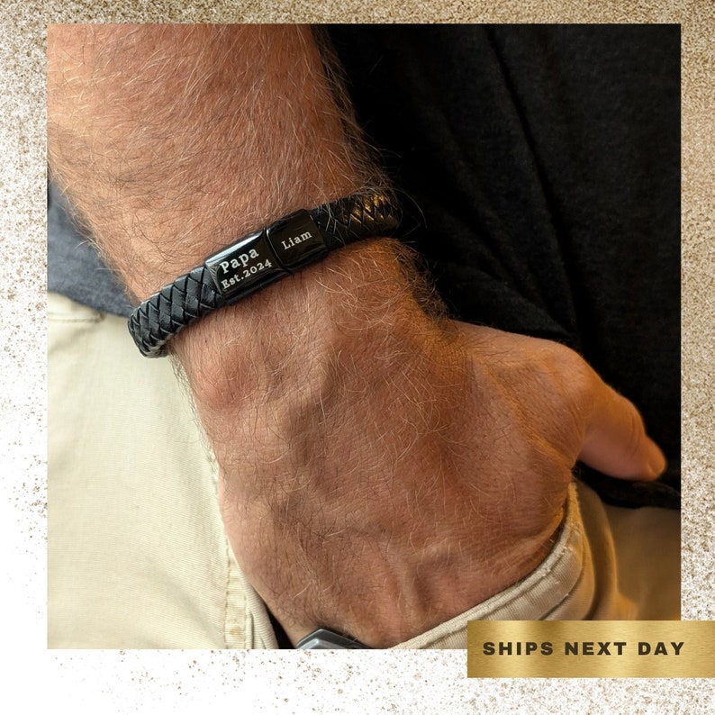 Personalized Black Leather Bracelet for Men – Engraved Magnetic Clasp | Custom Gift for Husband, Boyfriend or Dad, Custom Father's Day name. Close-up image of a man's wrist wearing a black braided leather bracelet engraved with the words "Papa Est. 2024" and "Liam" on two metal plates. The bracelet has a masculine, rugged style and is shown against a background of casual clothing. The bracelet is personalized and designed as a sentimental gift for new fathers or grandfathers.