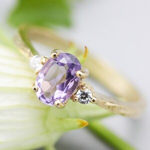 Oval faceted amethyst ring with tiny round diamonds side set gems in prongs setting with 14k gold texture band