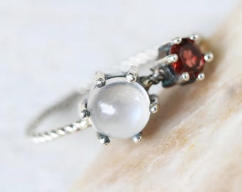 Round moonstone ring in silver bezel and prongs setting and tiny garnet on the side with sterling silver twist design band