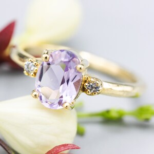 Oval faceted Amethyst ring with tiny round diamonds side set gems in prongs setting with 14k gold half round band