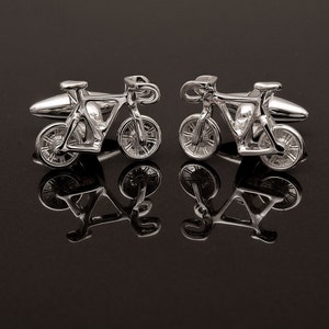 May include: A pair of silver cufflinks in the shape of a bicycle. The cufflinks are detailed and realistic, with a silver finish.