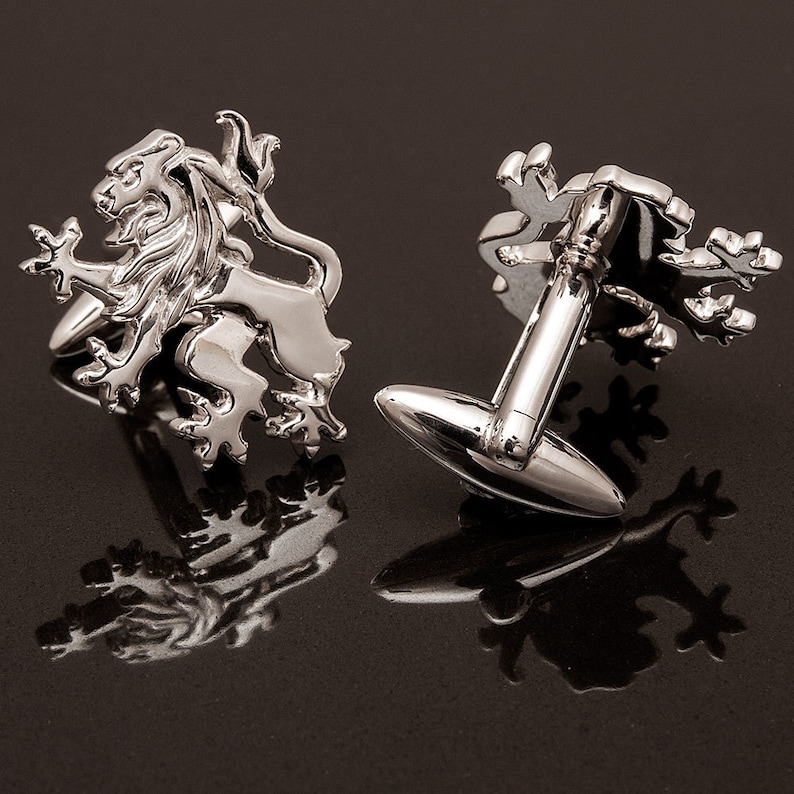 May include: A pair of silver cufflinks featuring a lion design. The cufflinks are shown on a black surface.
