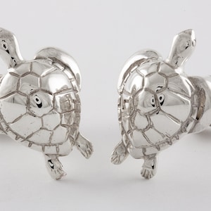 May include: A pair of silver turtle cufflinks. The turtles are facing each other and have detailed shell patterns.