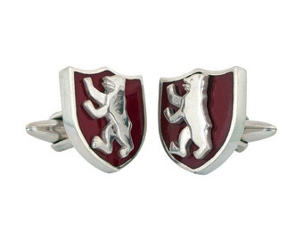 May include: A pair of silver cufflinks with a red enamel shield featuring a white bear. The bear is standing on its hind legs with its paws raised.