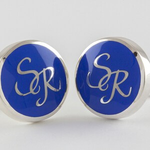 May include: A pair of silver cufflinks with blue enamel and the initials "SR" in silver.