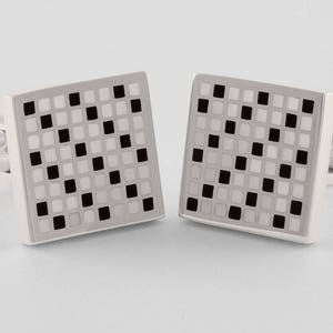 May include: A pair of silver cufflinks with a black and white checkered pattern.