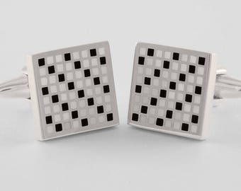 May include: A pair of silver cufflinks with a black and white checkered pattern.
