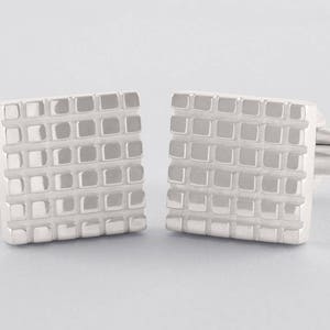 May include: A pair of silver cufflinks with a square design. The cufflinks have a textured surface with a grid pattern.