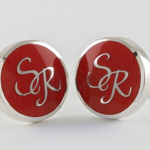 May include: A pair of silver cufflinks with red enamel and the initials "SR" engraved in white.