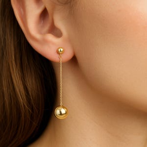 May include: Gold drop earrings with a small ball at the top and a larger ball at the bottom connected by a delicate chain.