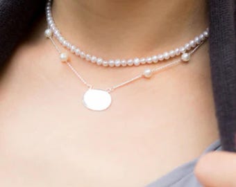 May include: A silver necklace with a round pendant and a pearl strand. The necklace is layered with a second strand of pearls.