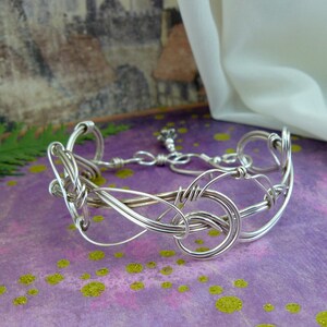 May include: A silver wire bracelet with a delicate, intricate design. The bracelet is made of multiple strands of wire that are woven together to create a unique and stylish look.