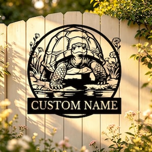 May include: A black metal circular wall sign featuring a detailed illustration of a tortoise walking through flowers. The design includes a rectangular banner at the bottom with the text CUSTOM NAME in a bold, capitalised, sans-serif font.