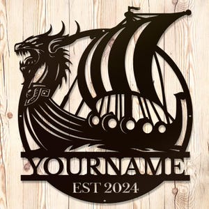 Puede incluir: Señal de metal negro con un diseño de barco vikingo y dragón. La señal incluye el texto "YOURNAME EST 2024".