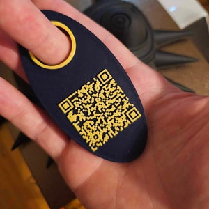 Puede incluir: Un llavero azul oscuro con un código QR amarillo y un anillo amarillo para un lazo de dedo.