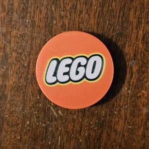 May include: A round, orange phone grip with the word "LEGO" in white letters with a yellow outline.
