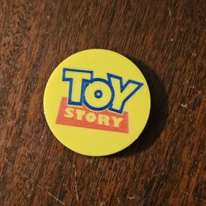 May include: A yellow round sticker with the words "TOY STORY" in blue and red letters.